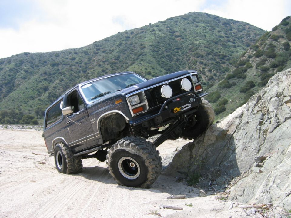 Lifted dark blue Ford Bronco with big mud tires climbing a rock in a mountain wash