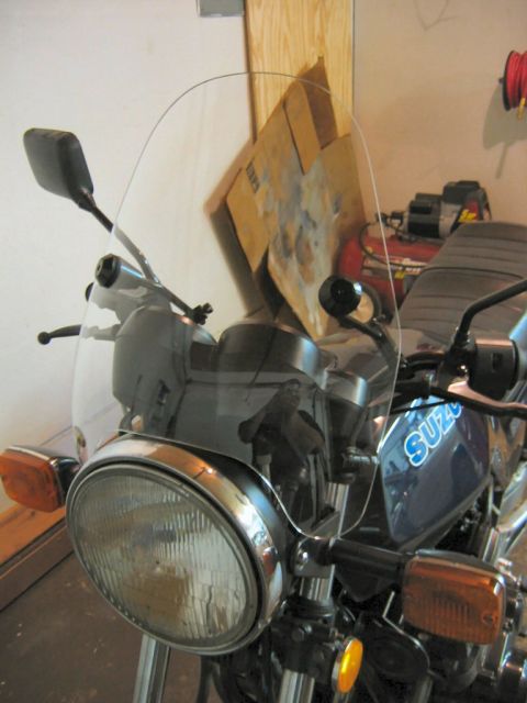 1985 Ford LTD Crown Victoria - A motorcycle's front view shows a clear windscreen and a blue fuel tank with the "SUZUKI" logo visible.