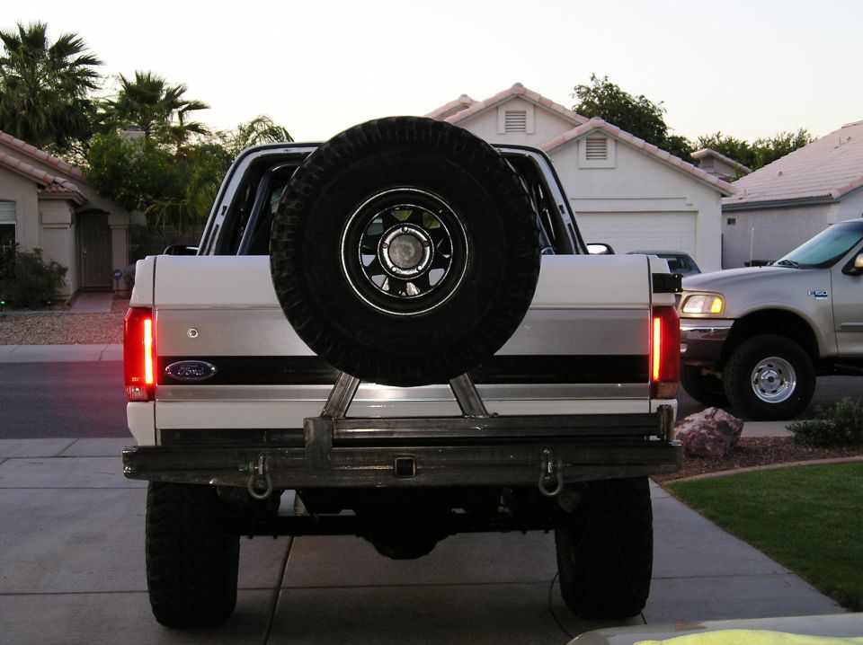Rear of a topless white Ford Bronco with custom steel bumper and center spare tire carrier at dusk