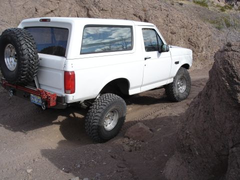 1996 Ford Bronco - This white SUV is equipped with large tires and a spare on the rear, navigating a rocky, off-road path.