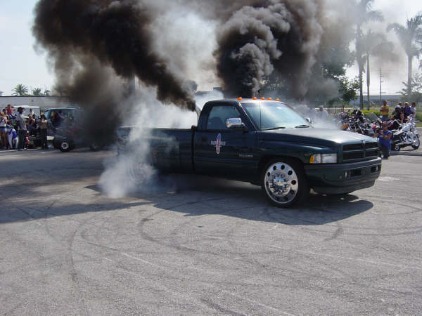 Green Dodge Ram dually pickup doing a burnout with heavy black smoke from exhaust stacks in a parking lot