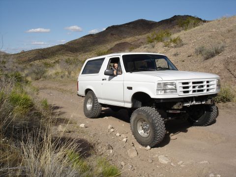 1996 Ford Bronco - A white 1996 Ford Bronco navigates a dusty trail with a driver visible inside.