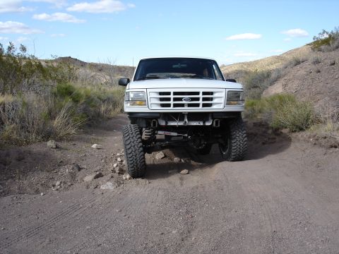 1996 Ford Bronco - A white Ford Bronco is shown from the front on a dirt road in a dry, hilly landscape.