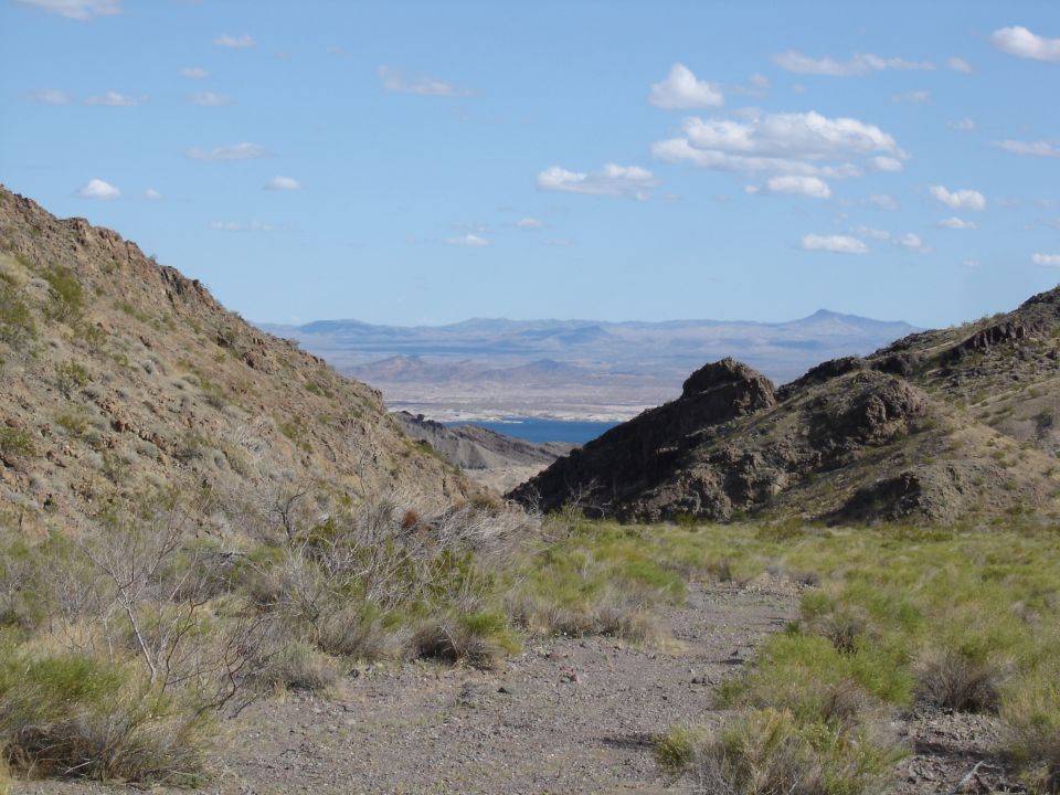 Desert landscape with mountains and a distant body of water under a blue sky