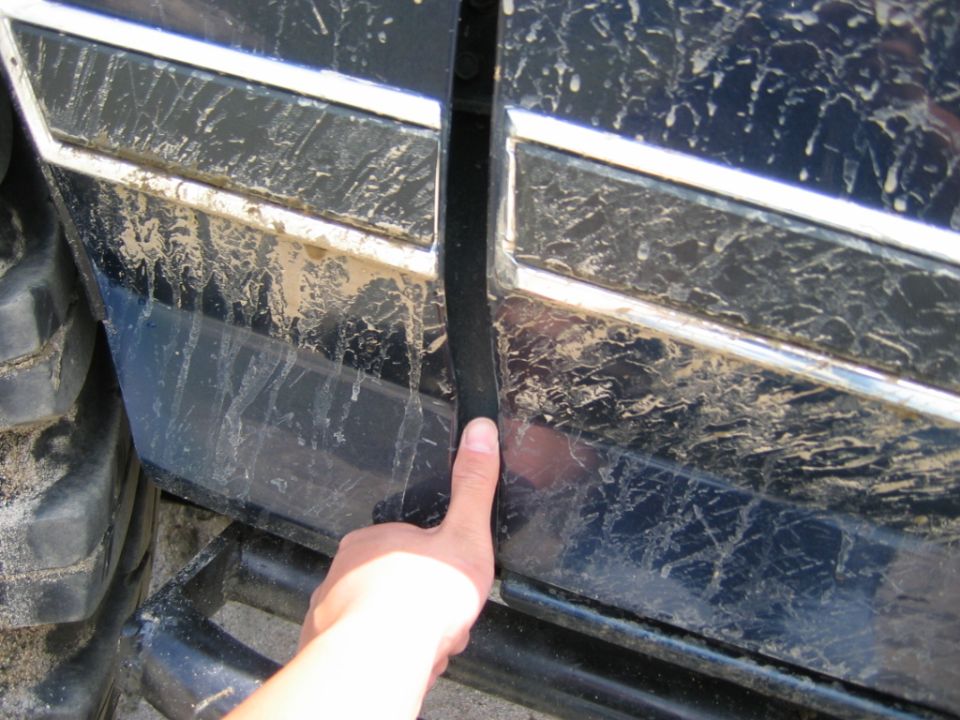 Hand pulling black trim on a dirty dark blue vehicle body panel with chrome strips