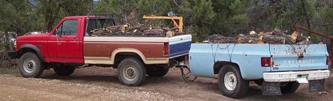 1990 Ford Bronco - Two pickup trucks, one towing the other, are loaded with firewood in a rural setting.