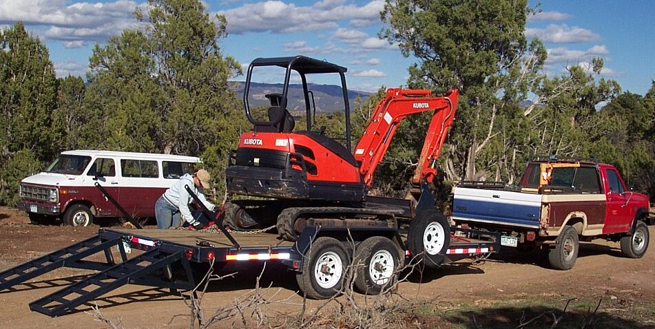 Kubota mini excavator strapped on trailer behind a red and tan Ford pickup