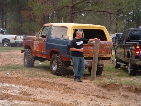 1993 Ford Bronco - A man in a 'Security' t-shirt stands by a weathered Ford Bronco in a muddy outdoor area.