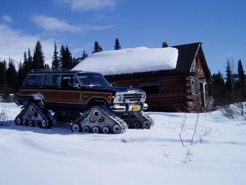 2000 Ford E350 - A vintage Jeep Grand Wagoneer equipped with snow tracks sits in a snowy landscape next to a rustic log cabin.