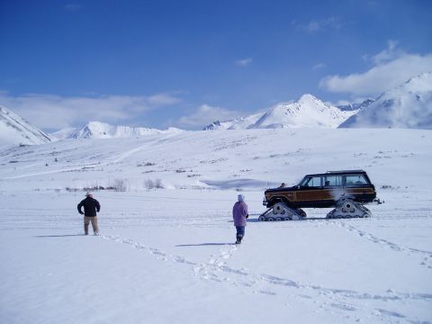 2000 Ford E350 - A station wagon equipped with snow tracks navigates a vast, snow-covered terrain under a clear blue sky.