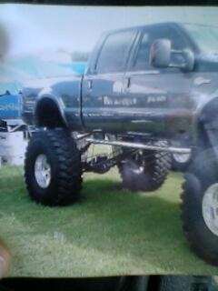 1995 Ford F-250 - This lifted pickup truck has massive tires and is parked on grass.