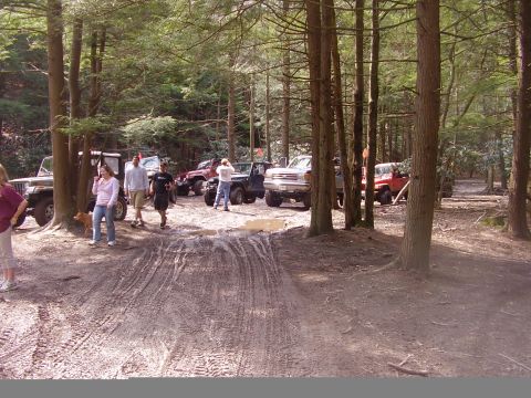 2003 Jeep Wrangler - A group of off-road vehicles are gathered in a wooded area, with several people present.