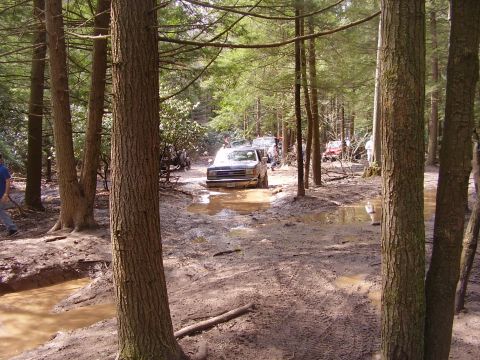 2003 Jeep Wrangler - Several off-road vehicles are seen driving through a muddy and wet forest path.