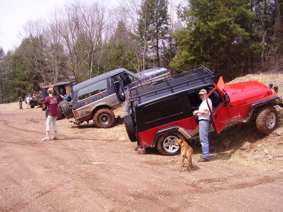 Red 2003 Jeep Wrangler Rubicon and a blue SUV on a dirt trail with trees in the background