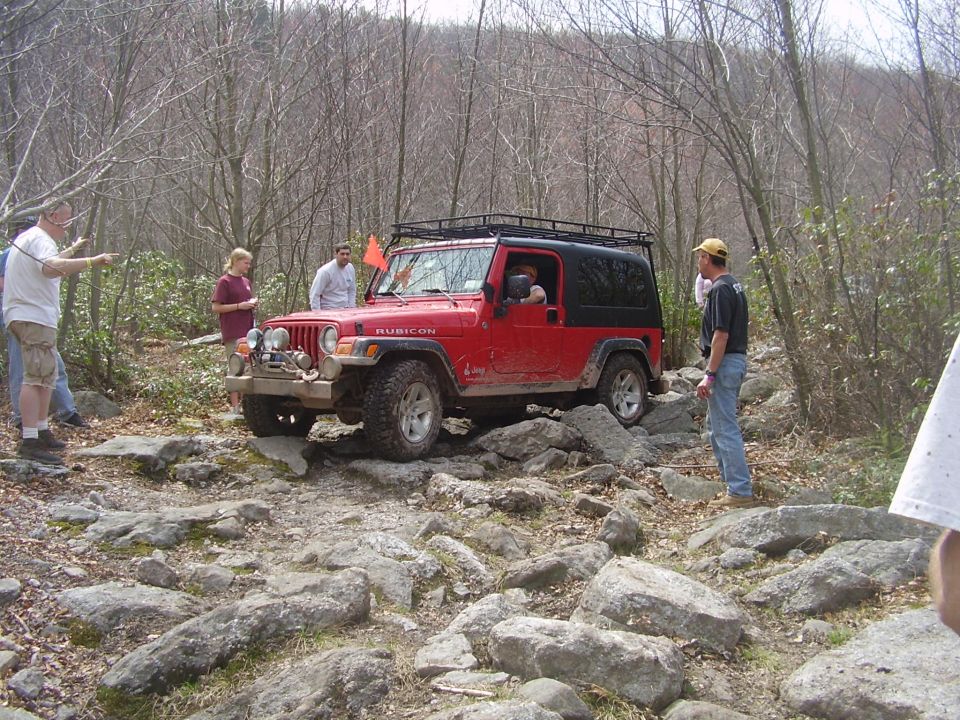 Red 2003 Jeep Wrangler Rubicon off-roading on a rocky trail with people watching