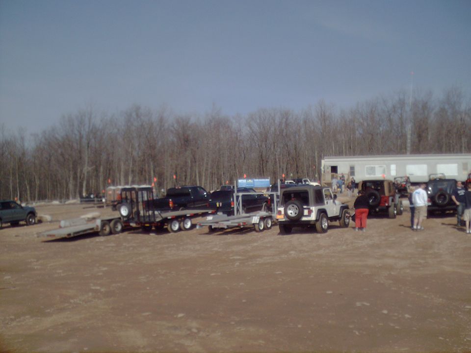 Several trucks and Jeeps parked in an outdoor lot with trailers and a building in the background