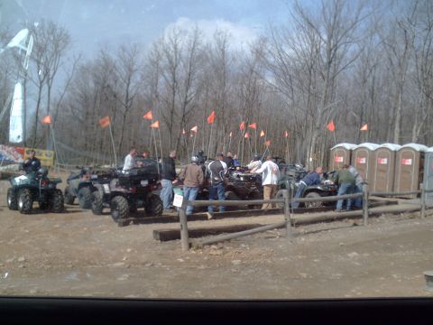 1991 Ford Bronco - Several ATVs are parked in a dirt lot, with people milling about near portable toilets and trees.