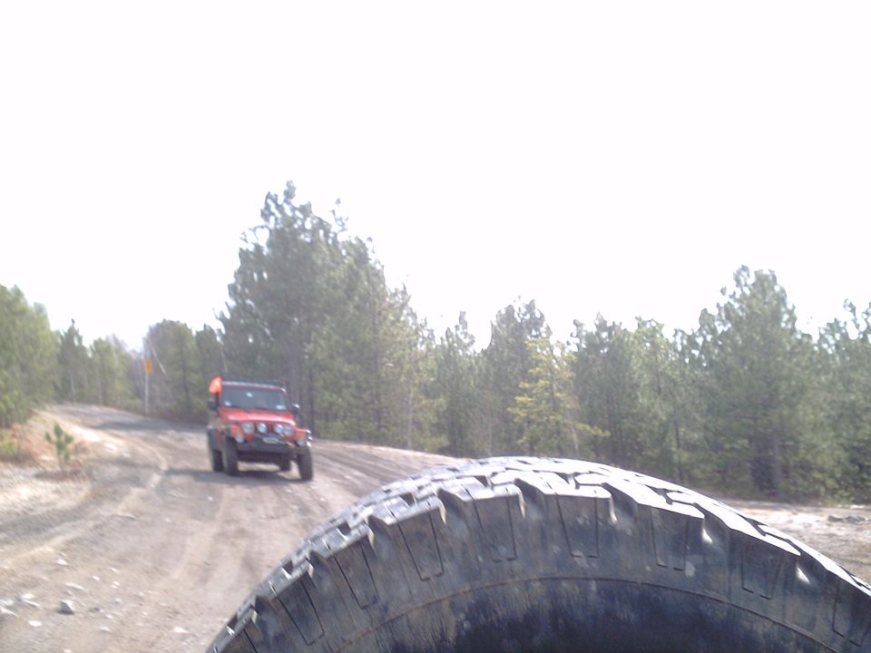 Red Jeep Wrangler on a dirt road, seen from another vehicle's tire