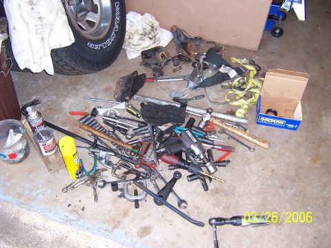 1987 Ford Bronco - Tools and parts are scattered on the garage floor, with a tire and suspension components visible.