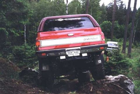 1995 Ford Bronco - This red Chevrolet SUV is navigating a challenging off-road course with a second vehicle visible in the trees.