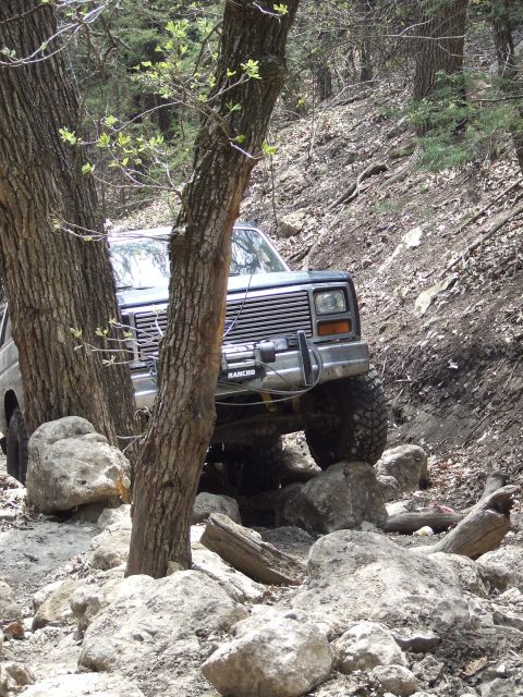 1986 Ford Bronco - 1986 Ford Bronco climbing over rocks on a wooded trail.