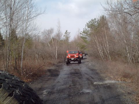 1991 Ford Bronco - A red SUV is seen from behind driving on a dirt road surrounded by trees in autumn.