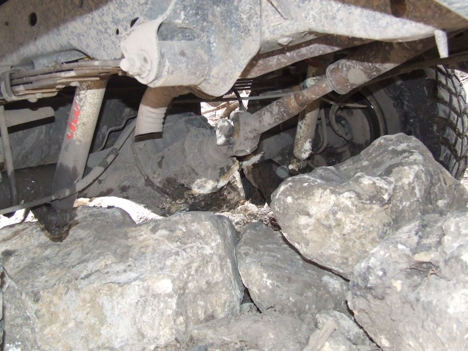Undercarriage of a vehicle, showing suspension and tire, resting on large rocks