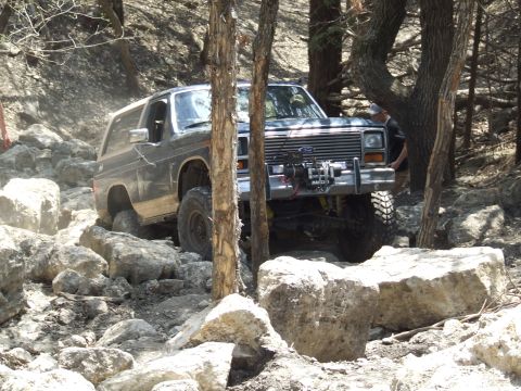 1986 Ford Bronco - This SUV is tackling a difficult off-road course with large rocks and trees.