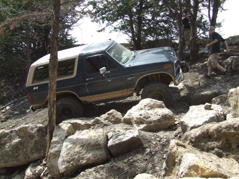 1986 Ford Bronco - A Ford Bronco navigates a rocky off-road course with trees and people in the background.