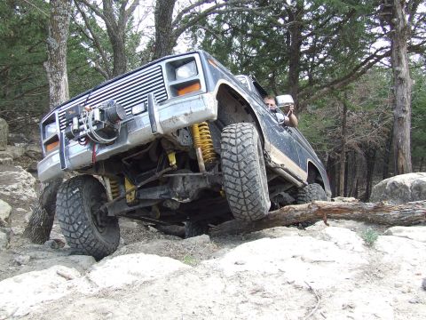 1986 Ford Bronco - Off-road vehicle with lifted suspension and large tires tackling a difficult rocky trail.