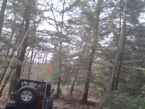 1991 Ford Bronco - A black Jeep Wrangler is seen from the rear on a muddy forest trail, with another vehicle partially visible behind it.