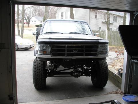 1994 Ford Bronco - This lifted Ford truck is parked inside a garage, showing its front end and suspension modifications.