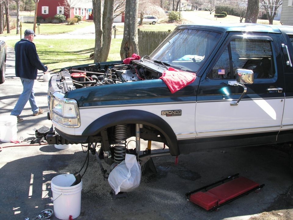 Man working on a 1994 Ford Bronco with the hood open and front end disassembled