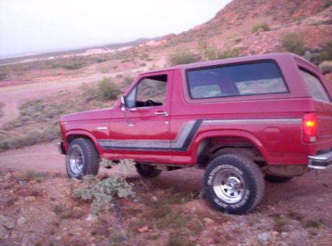 1993 Ford Bronco - A red SUV is parked on a dirt road in a dry, hilly landscape.