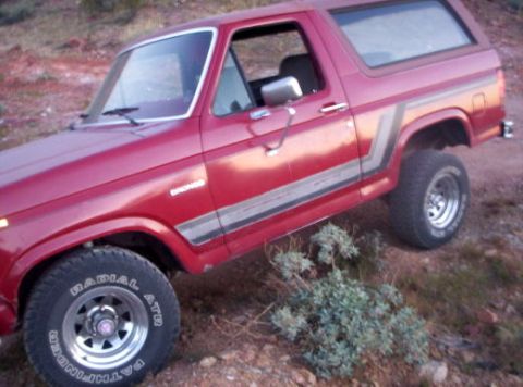 1993 Ford Bronco - This red Ford Bronco, likely from the early 1980s, is shown on a dirt incline with off-road tires.