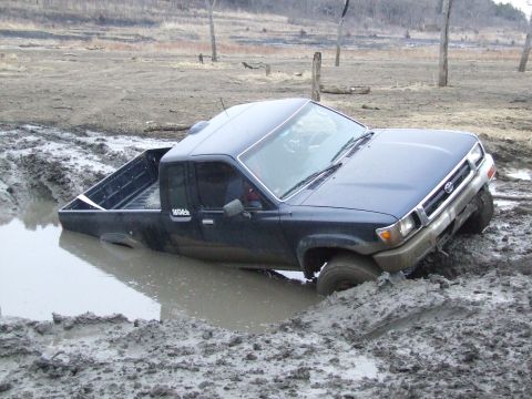 1986 Ford Bronco - This Toyota pickup truck is deeply stuck in a muddy area, with its front end submerged and angled downwards.