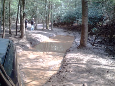 1991 Ford Bronco - A 1991 Ford Bronco navigates a challenging muddy path in a wooded area.