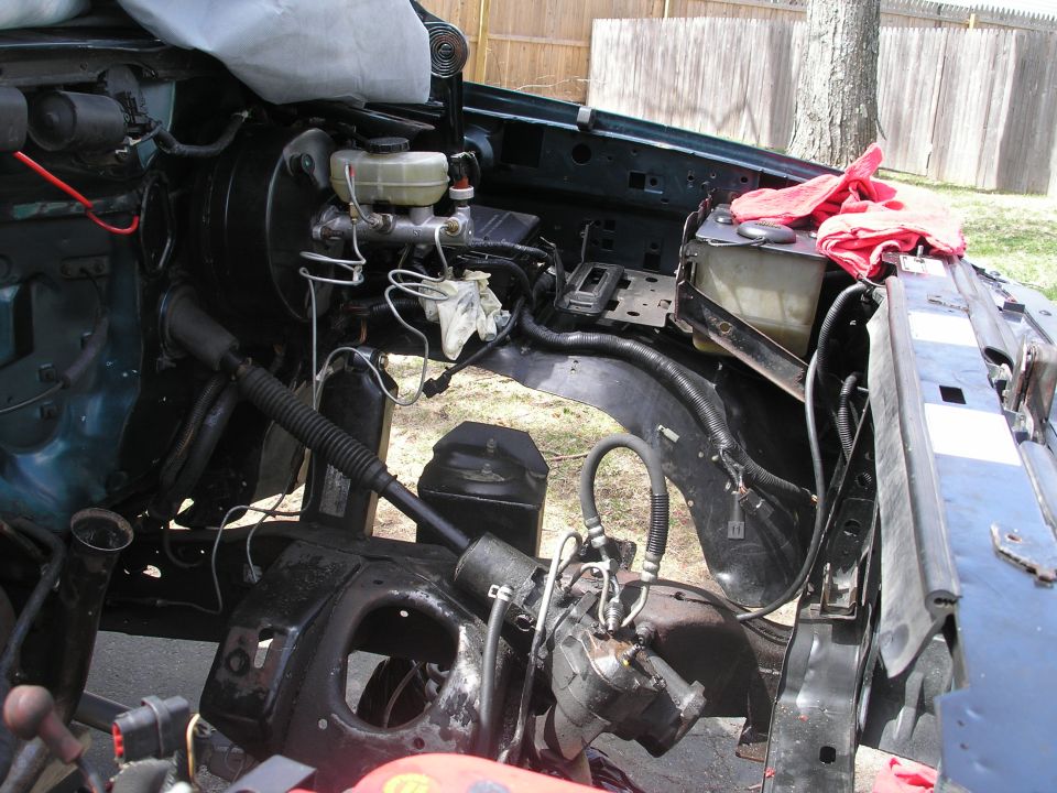 Engine bay of a dark green vehicle with brake booster, master cylinder, and steering components visible