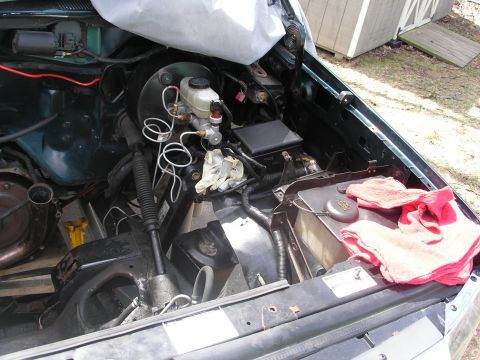 1994 Ford Bronco - The engine bay of a vehicle is shown with various components and wiring, partially covered by a tarp.