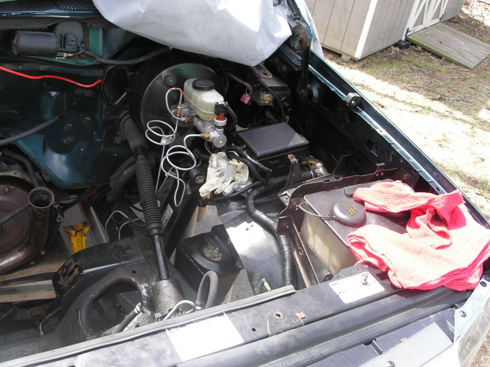 Engine bay with brake master cylinder, fuse box, and some wiring visible. A white tarp covers part of the engine