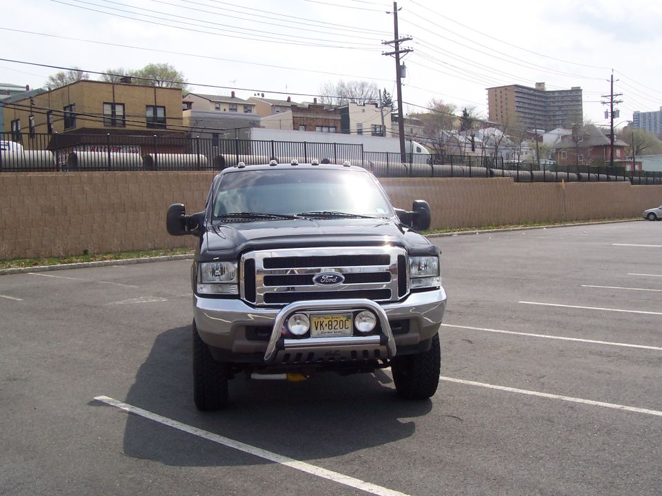 Front of dark gray lifted Ford SUV with chrome bull bar and NJ plate in a parking lot
