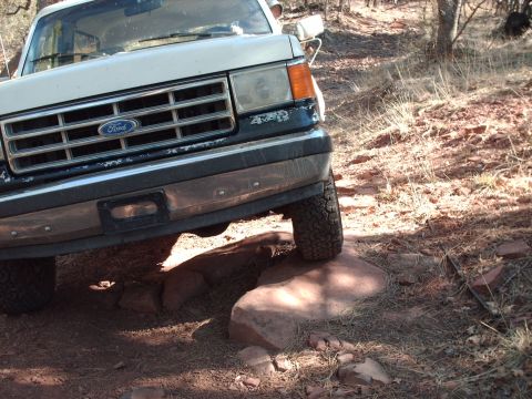 1988 Ford Bronco - A Ford truck navigates a rocky trail, with one tire placed on a large boulder.