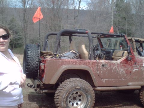 1991 Ford Bronco - A red Jeep Wrangler, covered in mud, is parked outdoors with two orange flags visible.
