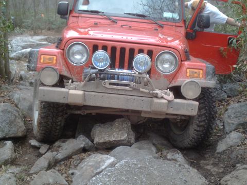 1991 Ford Bronco - A red Jeep Wrangler is shown off-roading on a challenging rocky path.