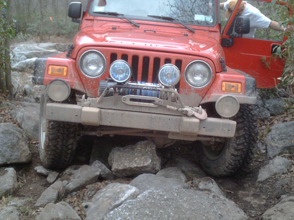 Red Jeep Wrangler navigating a rocky trail with a winch on the front bumper