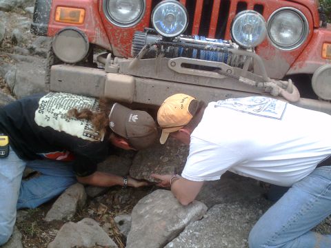 1991 Ford Bronco - Two people work to free a red Jeep Wrangler that is stuck on a rocky trail.