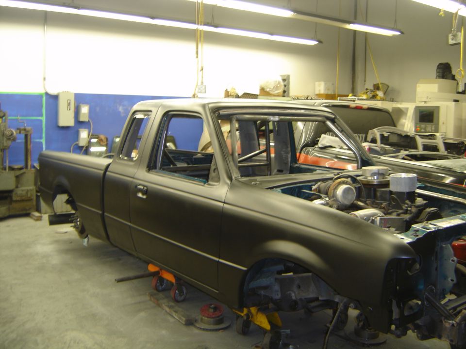 Flat black primered Ford Ranger extended cab on stands in a shop, no wheels or hood, diesel engine visible