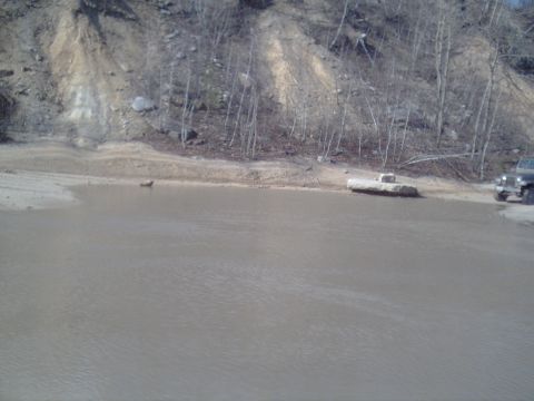 1991 Ford Bronco - A black Jeep Wrangler is parked on the muddy bank of a body of water.