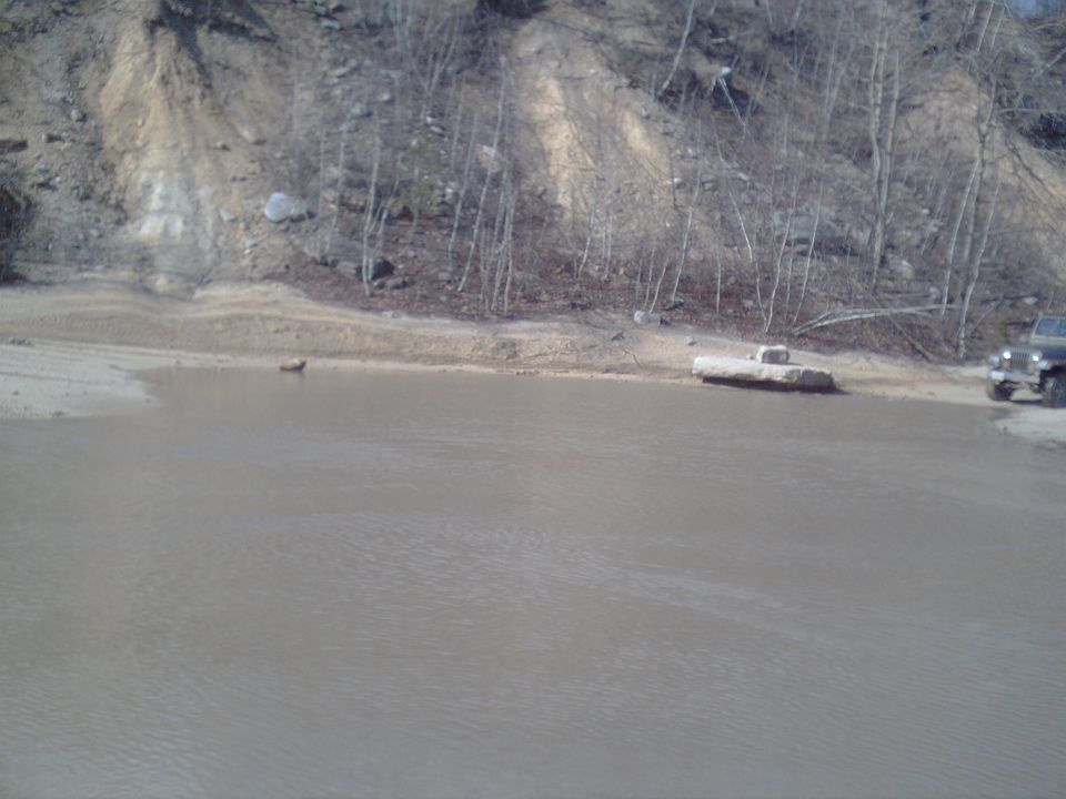 Black Jeep Wrangler parked on muddy shore near water