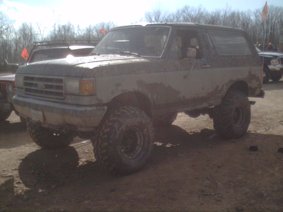 Mud-covered Ford Bronco with large tires, seen from the front-right